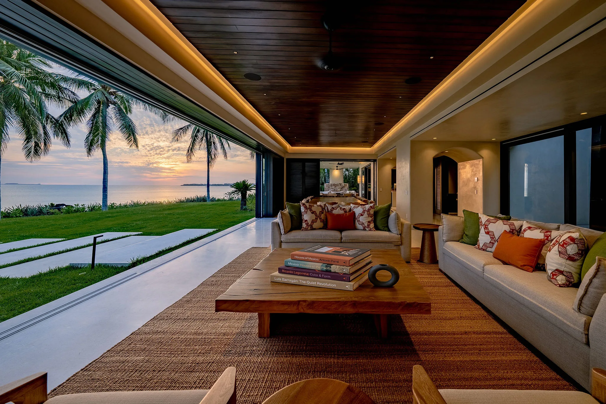 Open living room at Casa Happy Paws, Ranchos Estates: comfy sofas, glass doors to lawn, palms, and Punta Mita sunset.