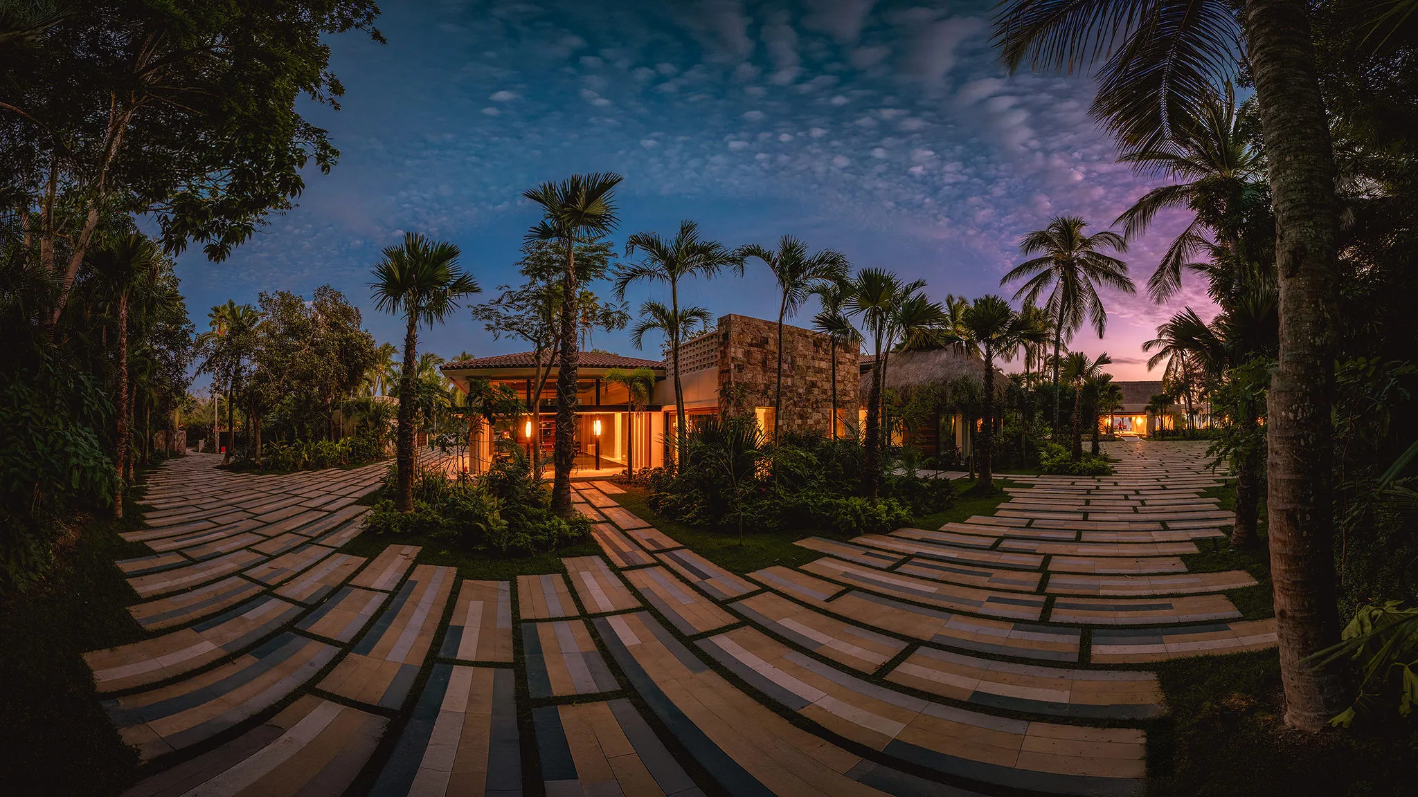 Casa Happy Paws in Punta Mita, Ranchos Estates, glows at dusk amid palms and greenery, with a curving tile path.