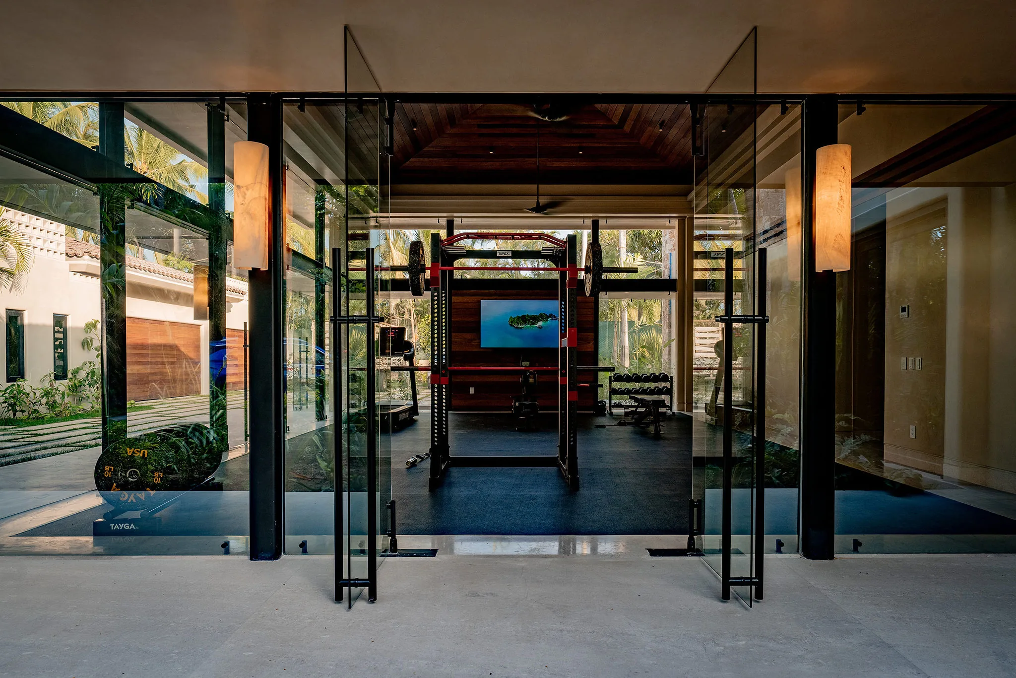 Contemporary home gym at Casa Happy Paws, Ranchos Estates, Punta Mita; glass walls, weights, lush views of Mexico greenery.