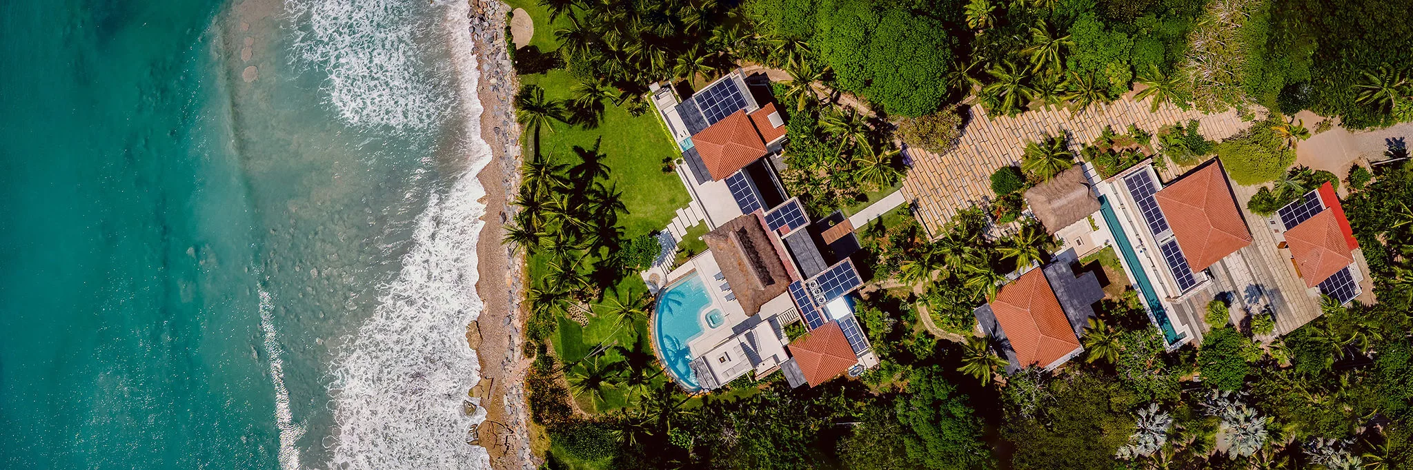 Aerial view of Casa Happy Paws, Punta Mita Ranchos Estates: red roofs, pool, solar panels, lush gardens by the ocean.