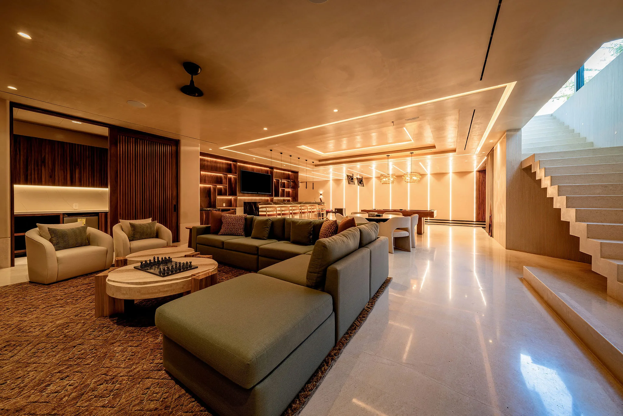 Modern Punta Mita living room with sectional sofa, armchairs, built-ins, chess set, TV, staircase, and natural light.