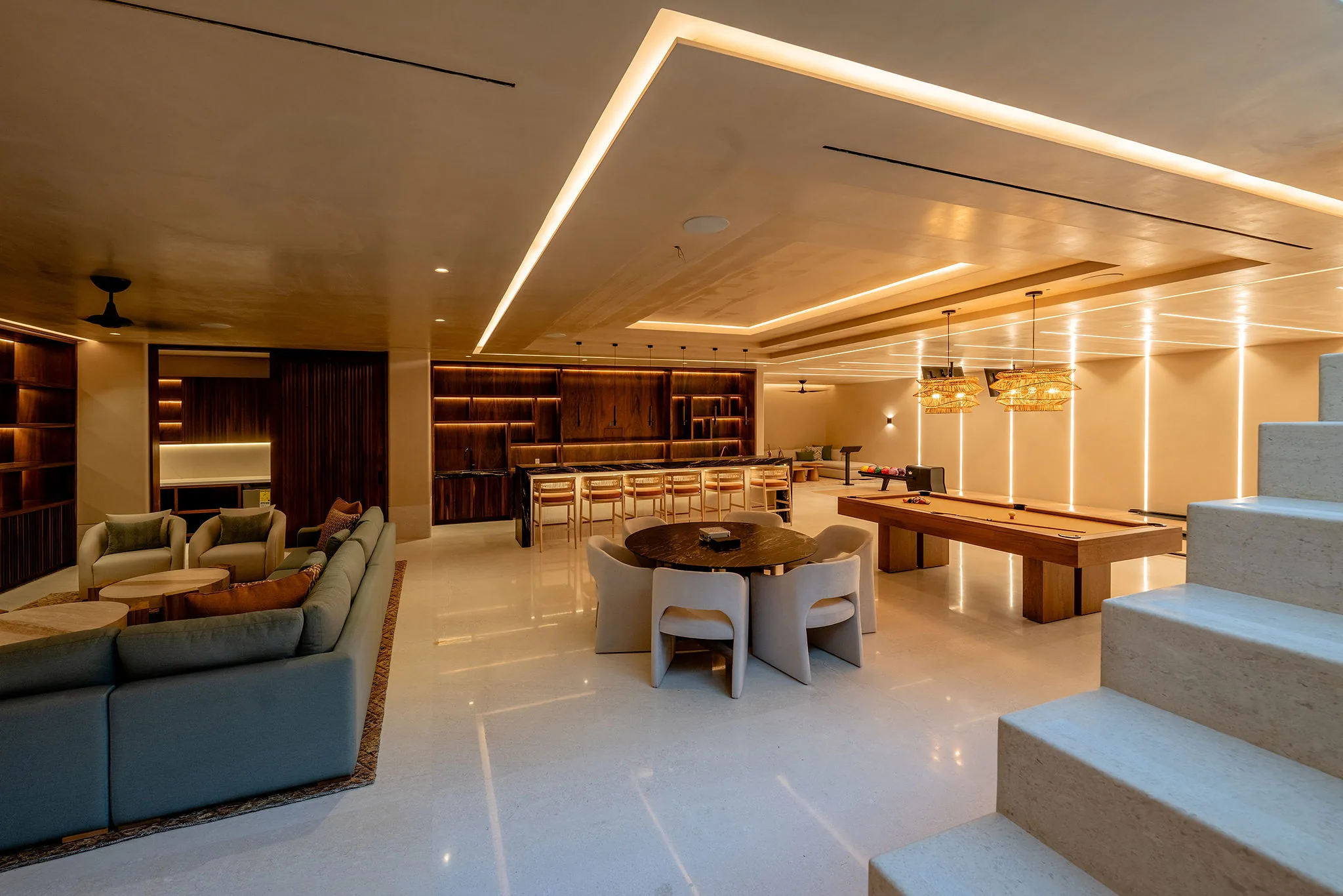 Modern basement in Punta Mita’s Ranchos Estates with pool table, bar, lounge seating, wooden shelves, and soft lighting.