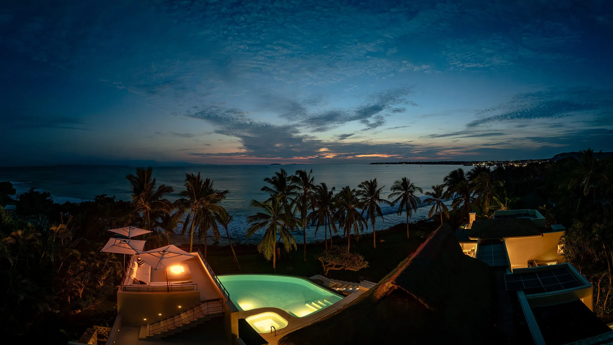 Casa Happy Paws at dusk in Punta Mita, Ranchos Estates—palm trees, glowing pool, ocean view, and dramatic blue sky.