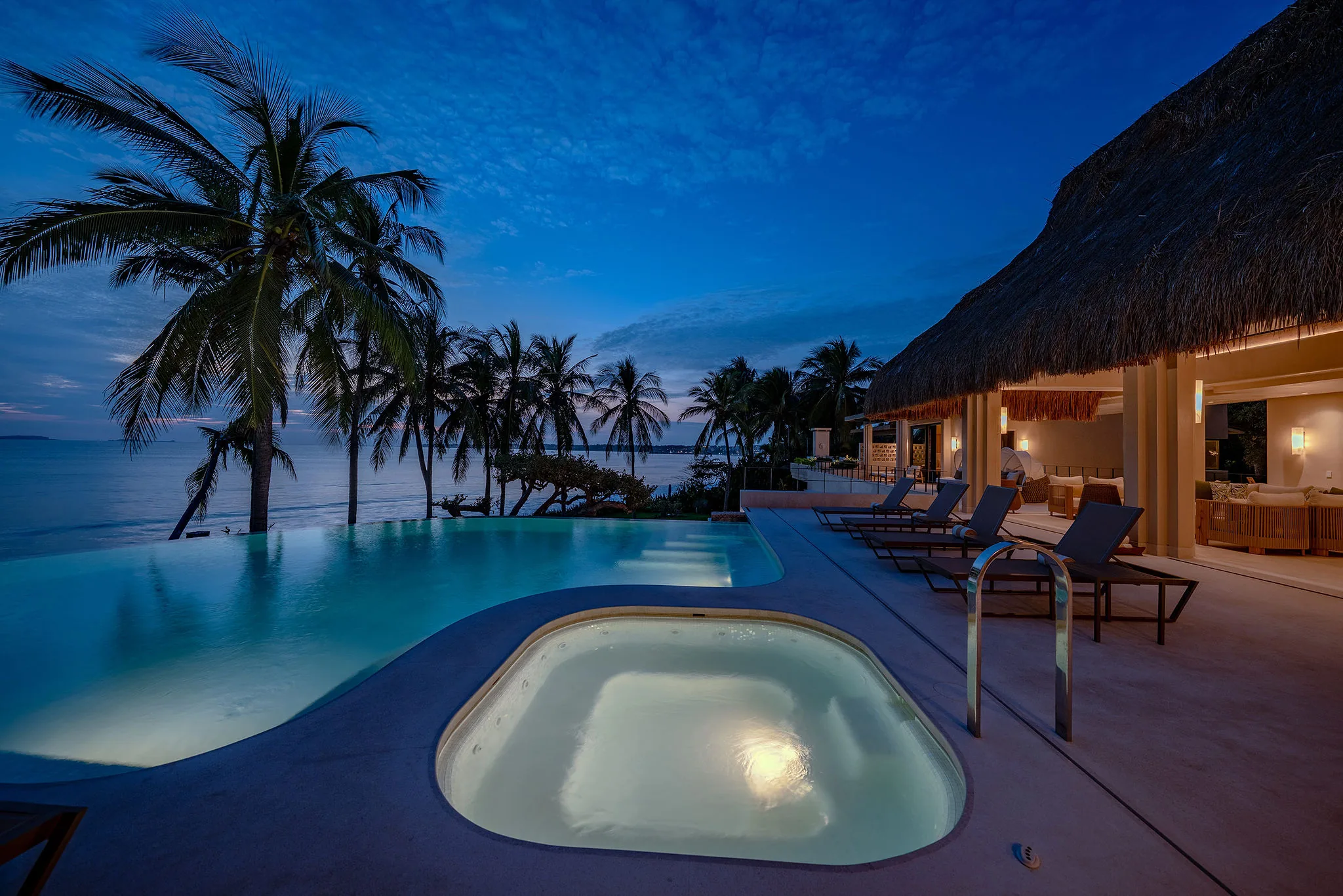 Casa Happy Paws, a Punta Mita Ranchos Estates beachfront resort, boasts oceanview pool, hot tub, palm trees, and glowing dusk lights.