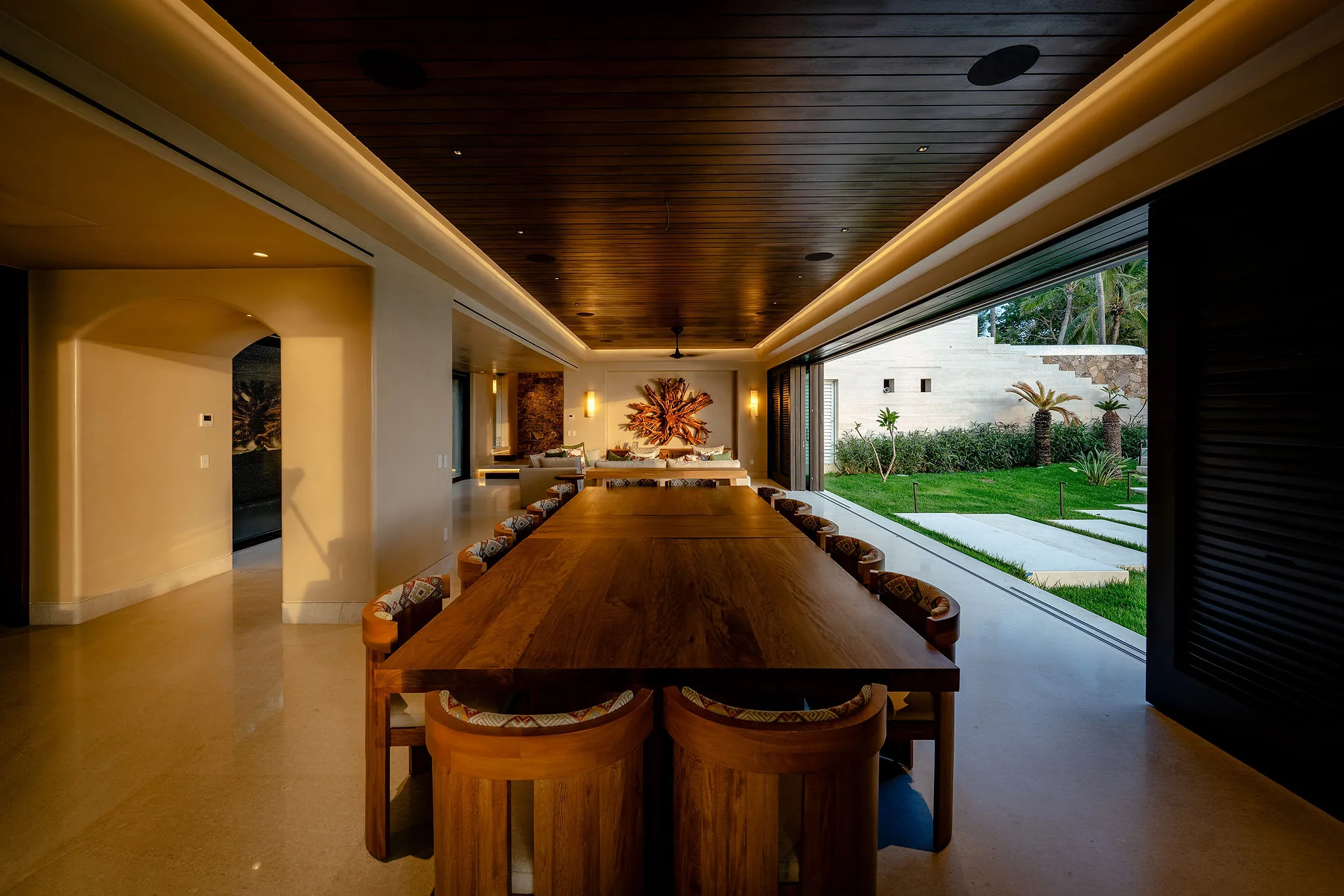 Dining room at Casa Happy Paws, Punta Mita—long table, warm lighting, wood ceiling, sliding doors to lush garden.