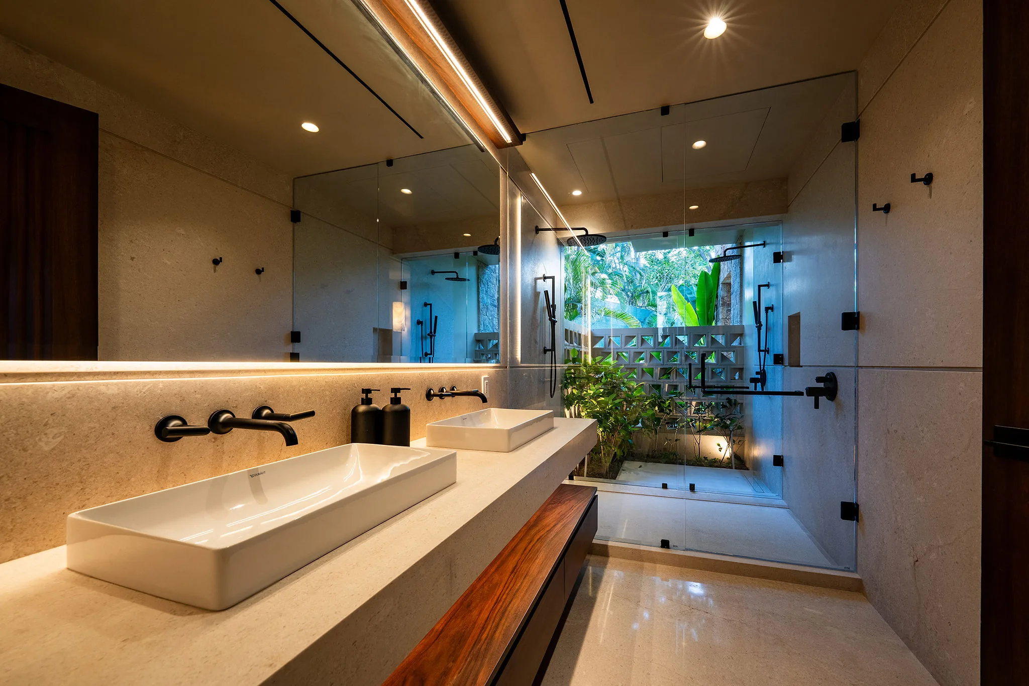 Modern bathroom at Punta Mita Ranchos Estates with beige walls, white sink, black fixtures, large mirror, and glass shower.