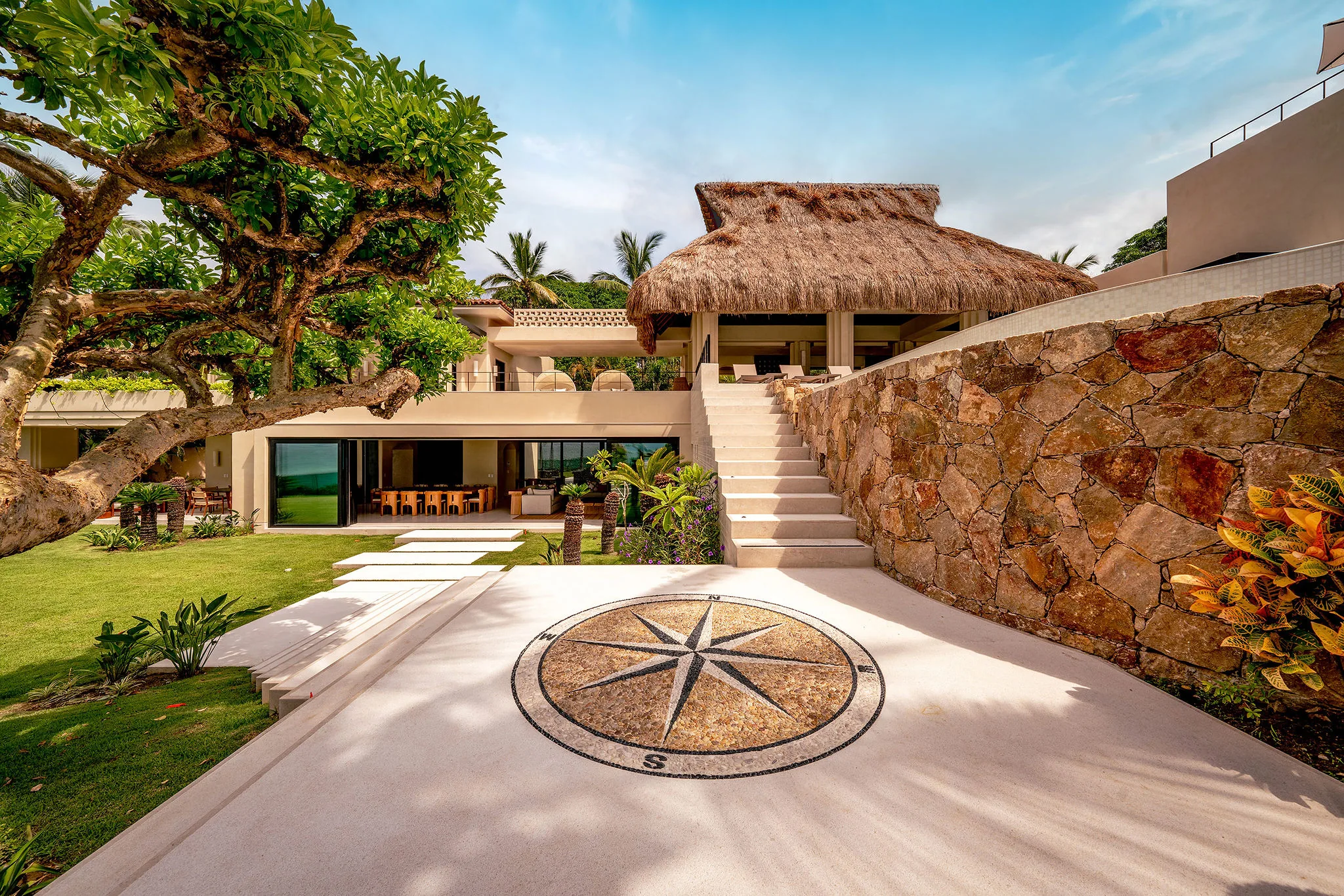 Casa Happy Paws in Punta Mita’s Ranchos Estates: thatched roof, stone walls, compass courtyard, lush greenery, outdoor stairs.