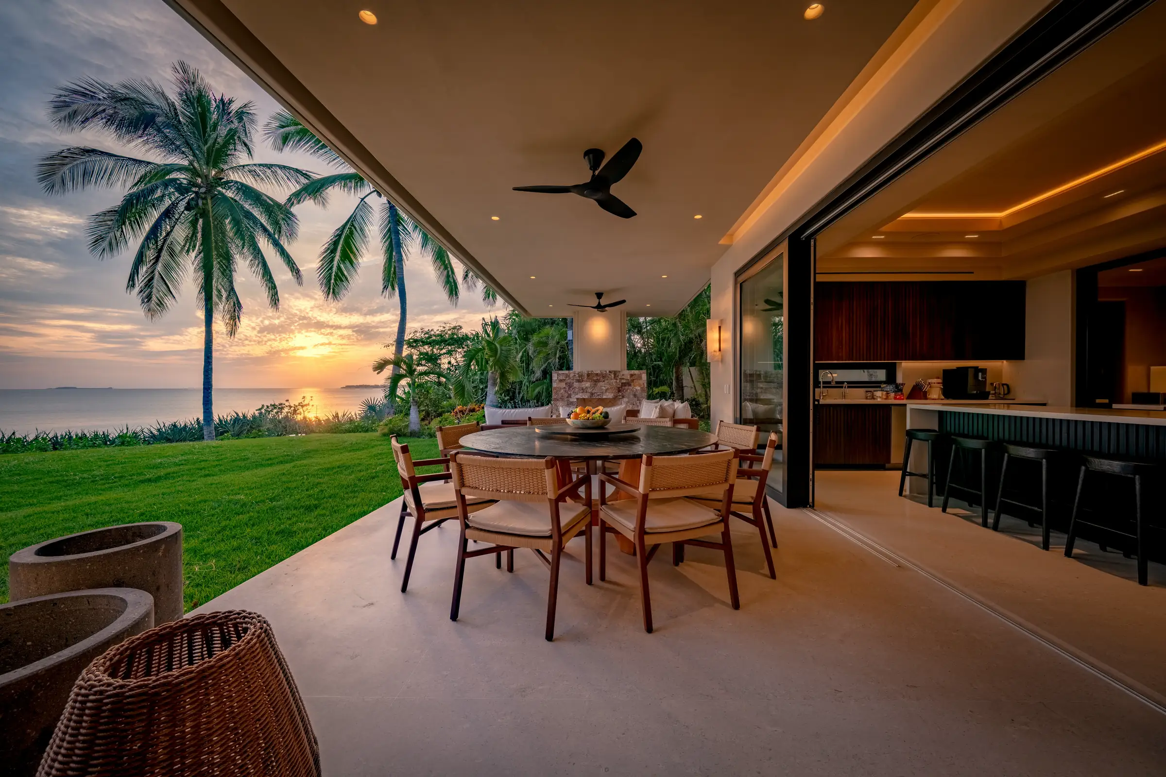 Open-air dining area at Casa Happy Paws, Ranchos Estates, Punta Mita; ocean sunset views, lush lawn, modern kitchen.