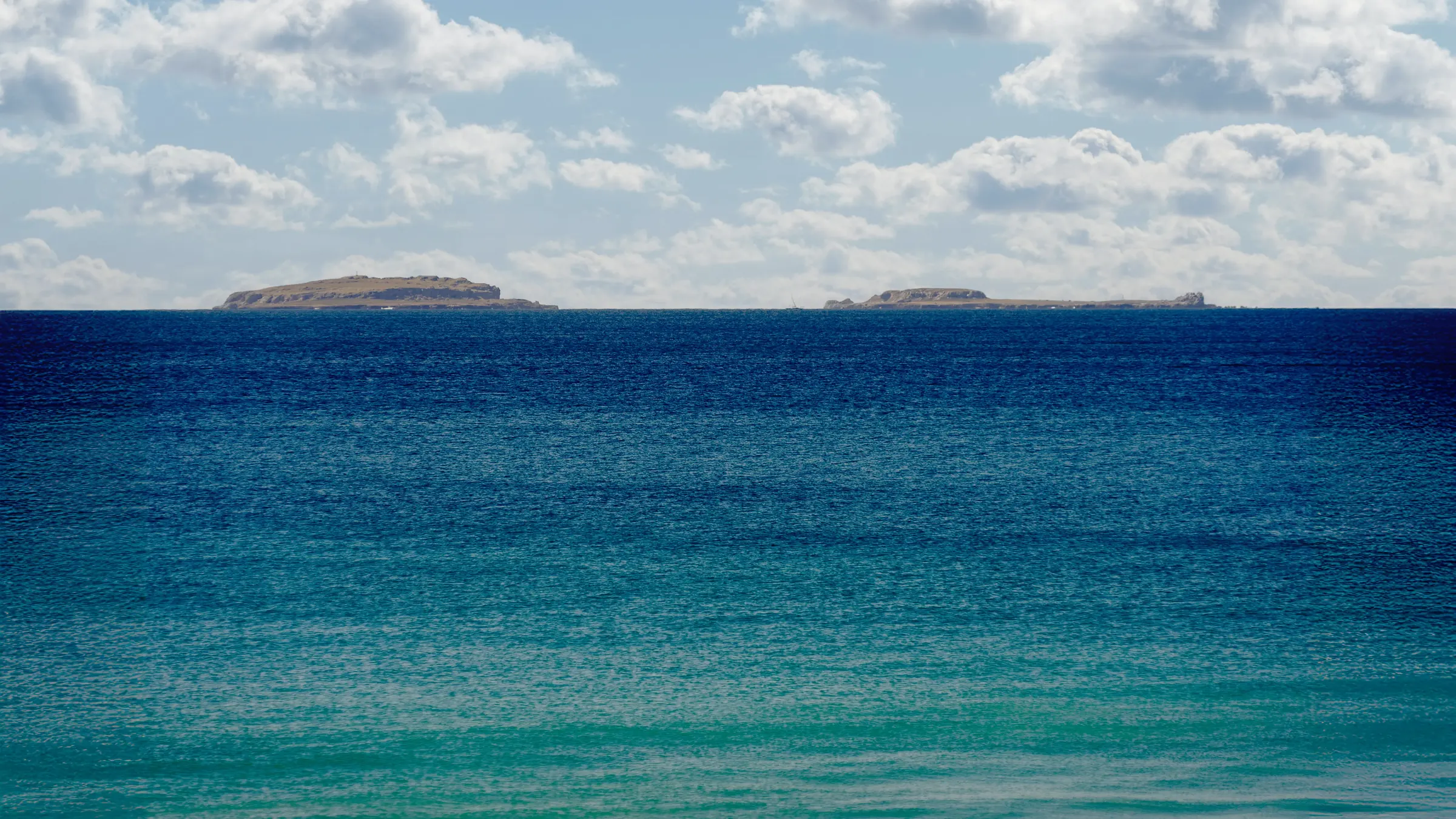 Tranquil Punta Mita coastline at Ranchos Estates: deep blue sea, turquoise shore, distant islands, and a partly cloudy sky.