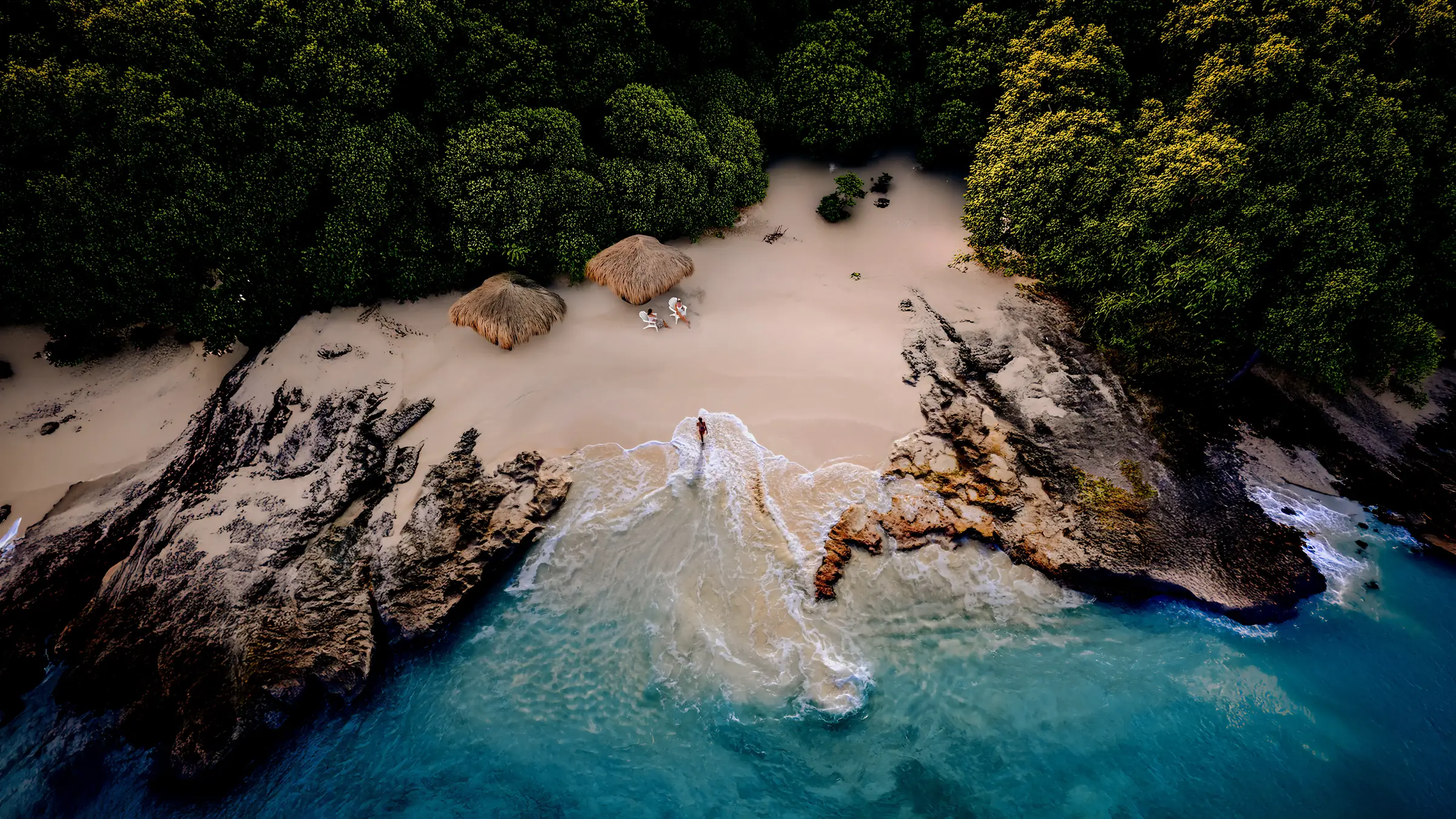 Aerial view of Punta Mita’s Ranchos Estates, Casa Happy Paws’ beachfront huts, lush trees, rocks and turquoise waves.