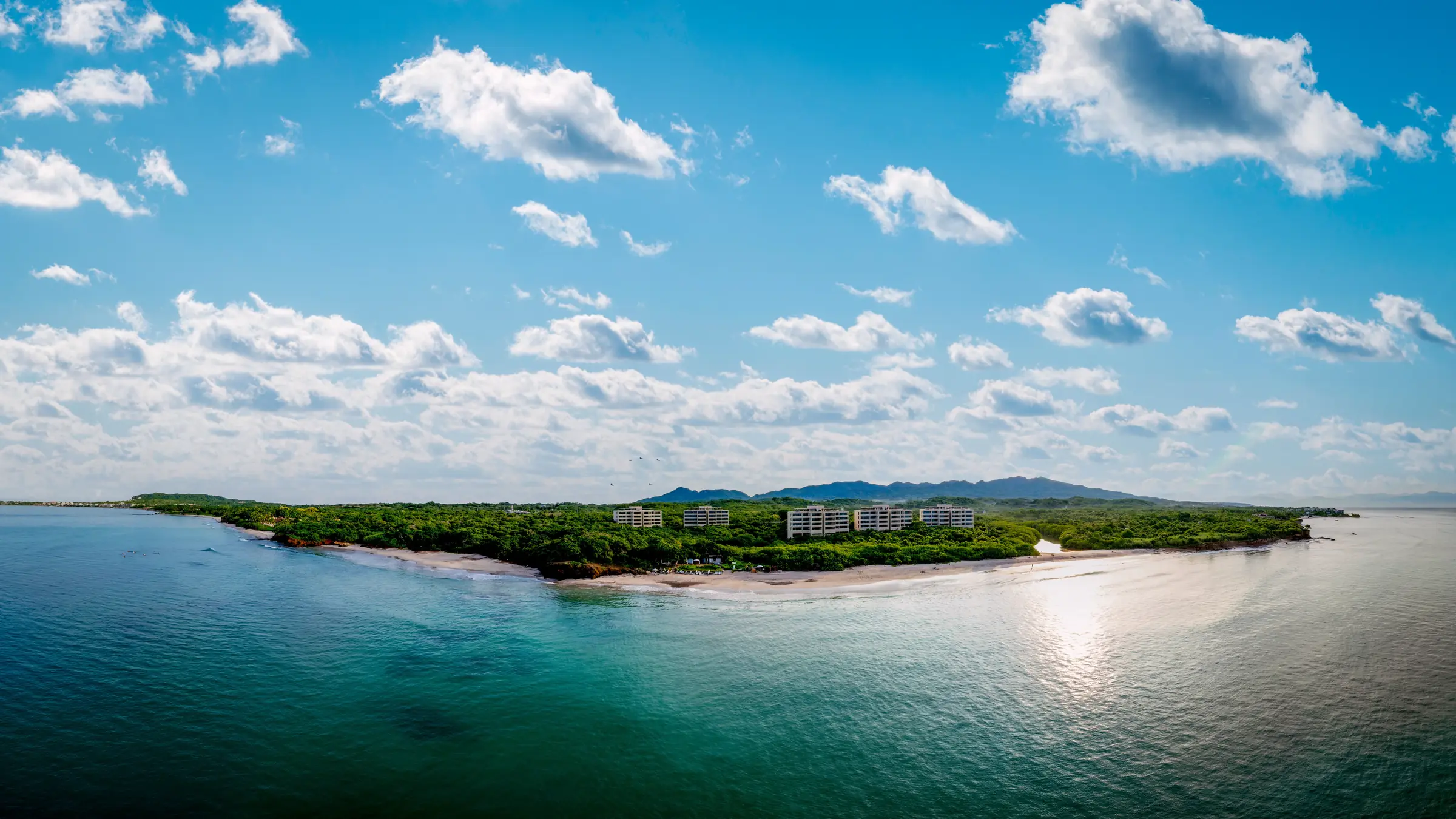 Panoramic view of Ranchos Estates, Punta Mita: turquoise water, sandy beach, lush trees, Casa Happy Paws nestled in greenery.