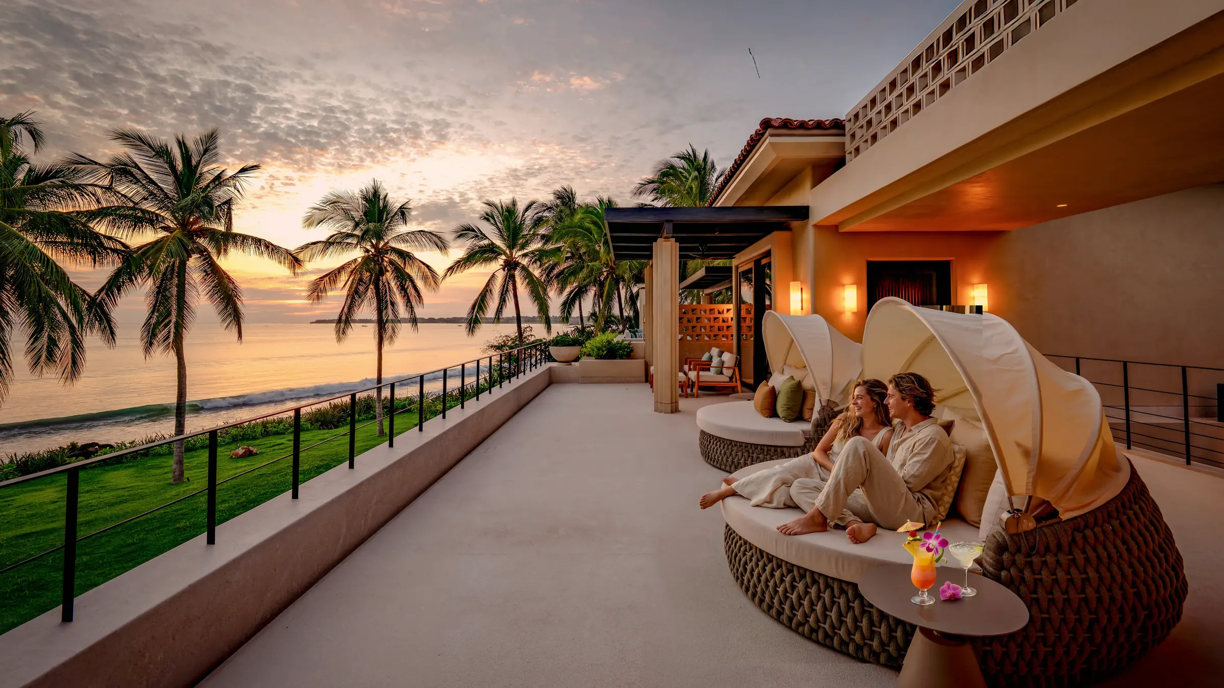 Guests in robes relax with tropical drinks at Casa Happy Paws, Ranchos Estates Punta Mita, at sunset on a palm-lined terrace.