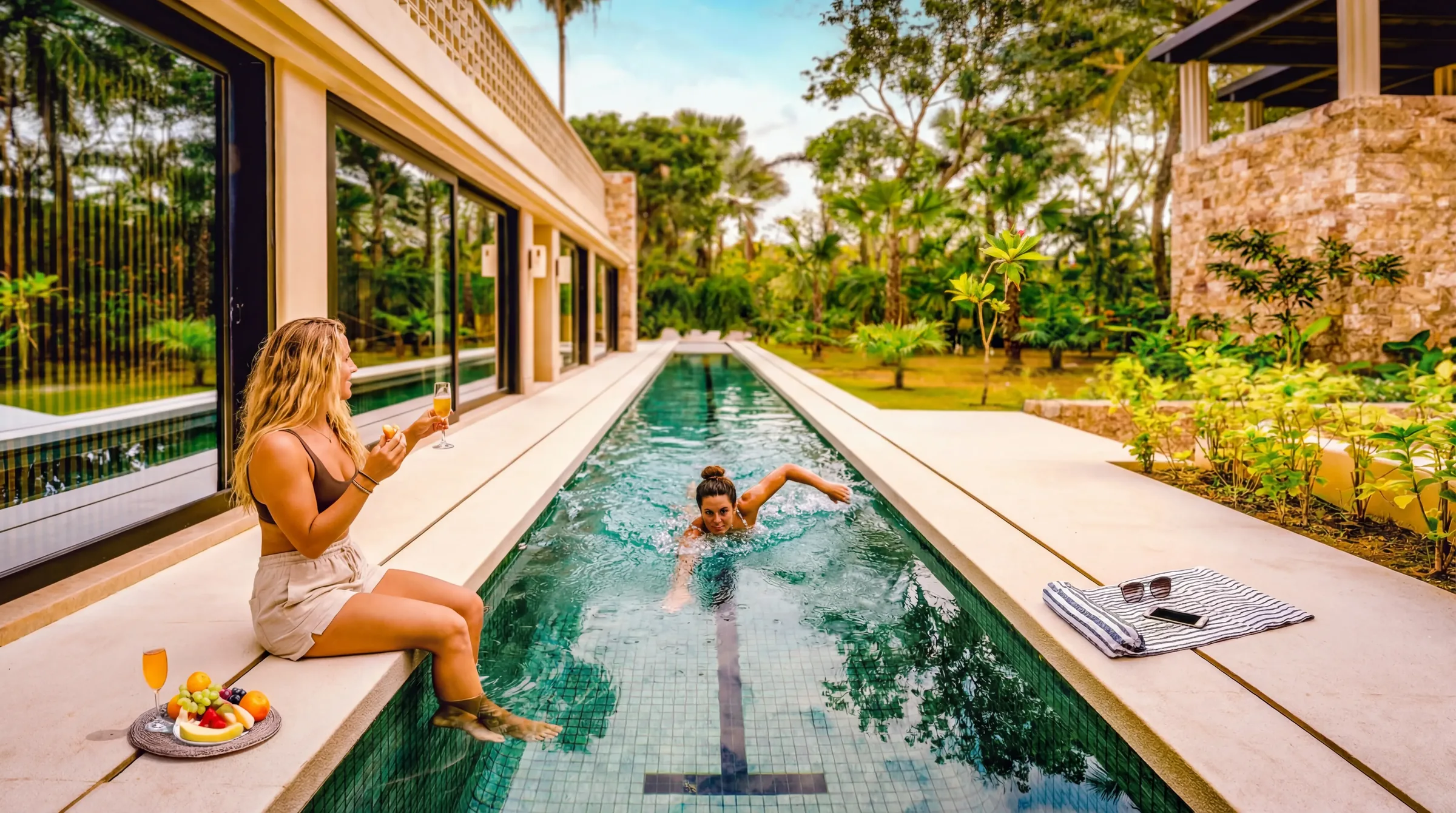 At Casa Happy Paws in Punta Mita’s Ranchos Estates, a woman lounges poolside with refreshments; lush, modern vibes abound.